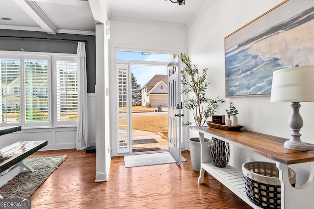 doorway with crown molding, a decorative wall, wainscoting, wood finished floors, and beamed ceiling