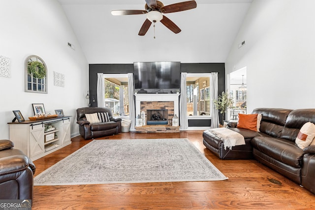 living area with visible vents, ceiling fan, a stone fireplace, wood finished floors, and high vaulted ceiling