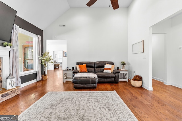 living room with a fireplace, a ceiling fan, wood finished floors, high vaulted ceiling, and baseboards