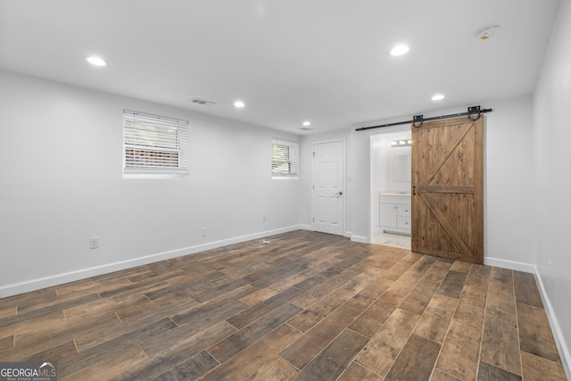 spare room featuring a barn door, recessed lighting, dark wood-type flooring, visible vents, and baseboards