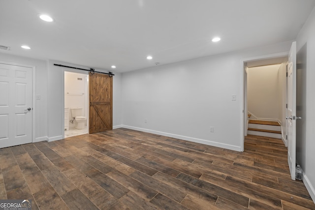 unfurnished room featuring a barn door, visible vents, dark wood finished floors, baseboards, and recessed lighting