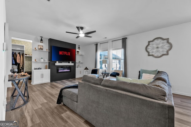 living area featuring light wood-style floors, visible vents, a ceiling fan, and a glass covered fireplace