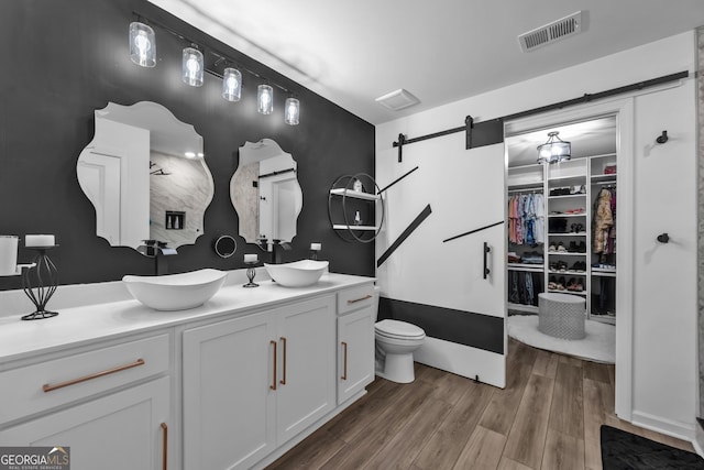 bathroom featuring wood finished floors, a sink, visible vents, a spacious closet, and double vanity