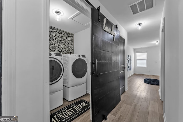 washroom with visible vents, a barn door, washing machine and dryer, wood finished floors, and laundry area