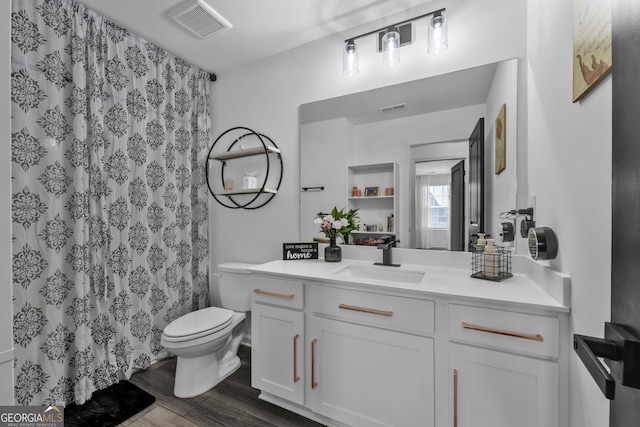 bathroom with toilet, vanity, wood finished floors, and visible vents