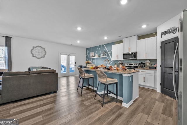 kitchen with open floor plan, appliances with stainless steel finishes, light wood-type flooring, and white cabinets