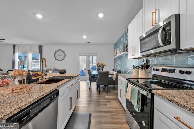 kitchen with light wood finished floors, backsplash, appliances with stainless steel finishes, white cabinetry, and a sink