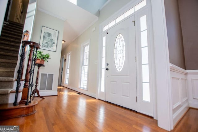 entrance foyer with stairs, visible vents, wood finished floors, and ornamental molding