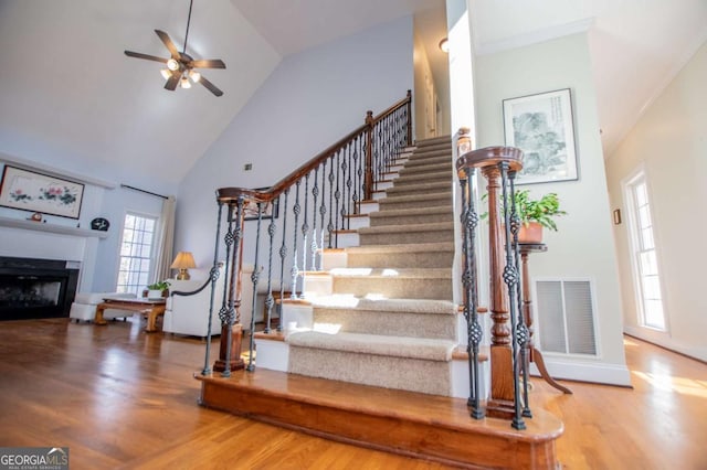 stairs featuring high vaulted ceiling, a fireplace, visible vents, and wood finished floors