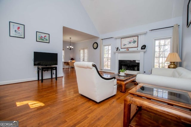 living room featuring high vaulted ceiling, a glass covered fireplace, wood finished floors, and a notable chandelier