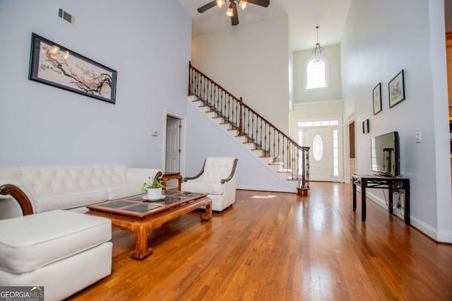 living room with wood finished floors, a towering ceiling, visible vents, stairs, and baseboards