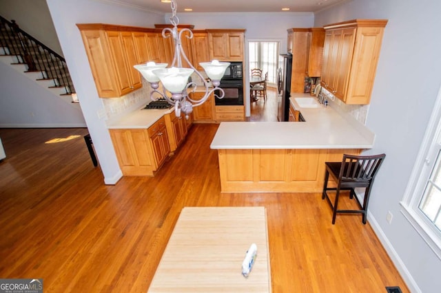 kitchen with a peninsula, a sink, light wood-style floors, black appliances, and tasteful backsplash