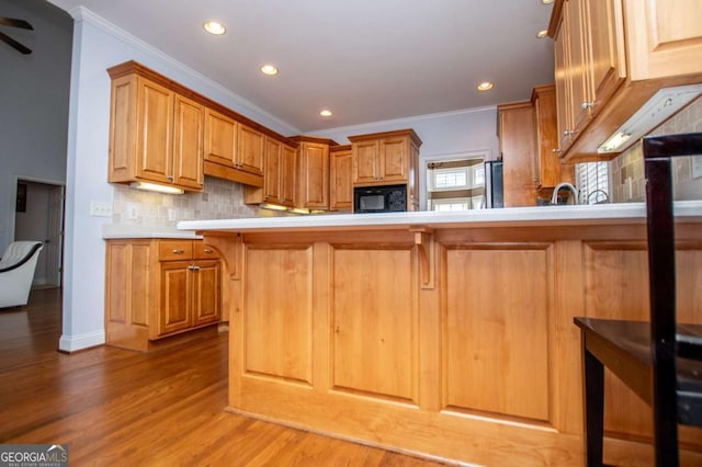 kitchen featuring black microwave, light countertops, crown molding, and decorative backsplash