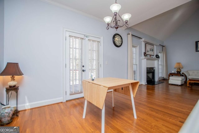 dining area with a fireplace, wood finished floors, baseboards, ornamental molding, and an inviting chandelier