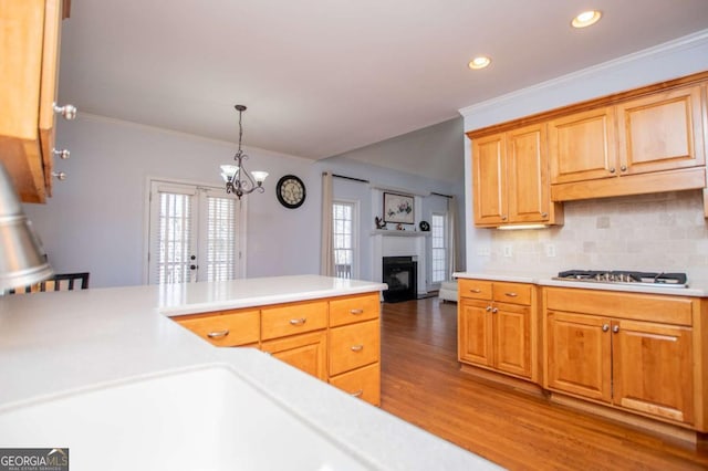 kitchen featuring crown molding, light countertops, stainless steel gas stovetop, decorative backsplash, and wood finished floors