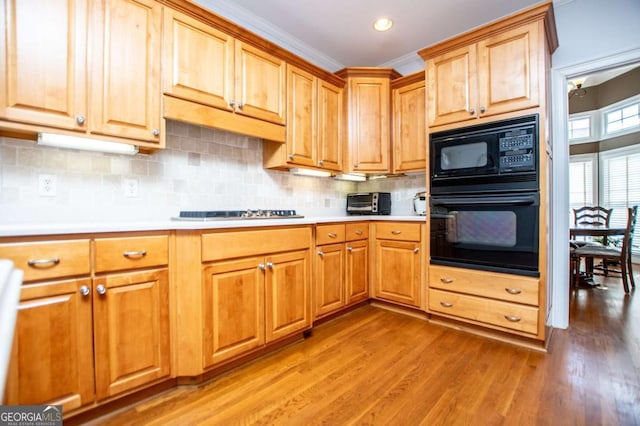 kitchen with black appliances, light wood finished floors, light countertops, and tasteful backsplash