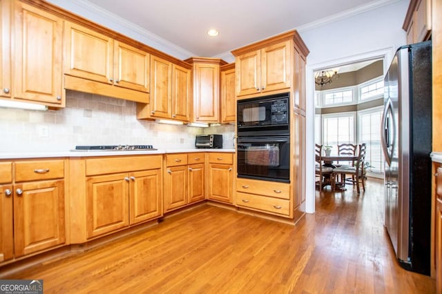 kitchen with light countertops, light wood-type flooring, backsplash, black appliances, and crown molding