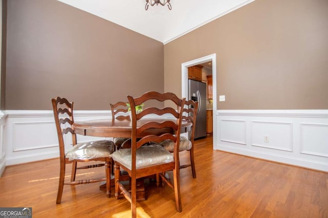 dining room featuring lofted ceiling, wainscoting, and light wood-style flooring