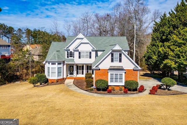 traditional-style home featuring a shingled roof, a front yard, brick siding, and driveway