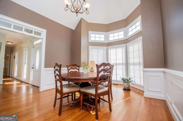 dining room with light wood finished floors, wainscoting, and an inviting chandelier