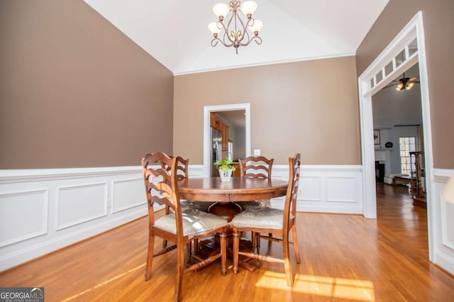 dining space with lofted ceiling, light wood-style floors, a fireplace, and a notable chandelier