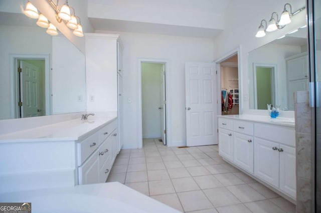 bathroom featuring baseboards, two vanities, a walk in closet, and tile patterned floors