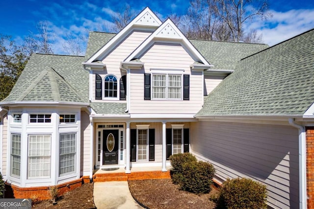 view of front of property with a garage, covered porch, and roof with shingles