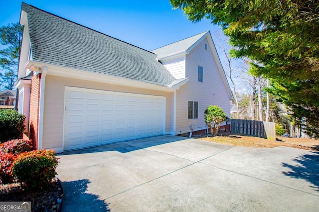 view of side of home featuring concrete driveway, roof with shingles, fence, and an attached garage