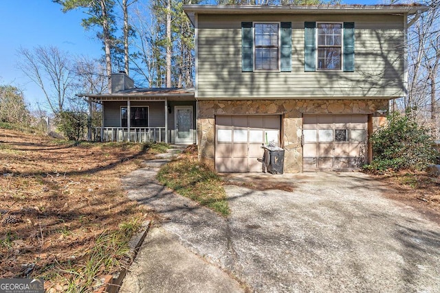 view of front of property featuring driveway, a garage, stone siding, a chimney, and covered porch