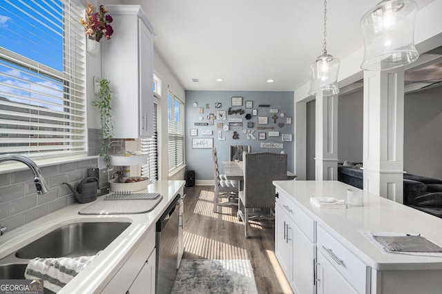 kitchen featuring tasteful backsplash, light countertops, stainless steel dishwasher, dark wood-type flooring, and a sink