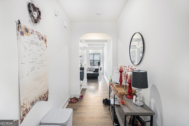 hall featuring arched walkways, wood finished floors, and baseboards