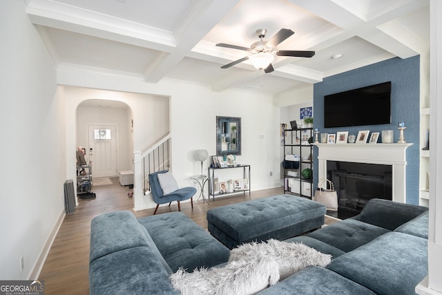 living area with arched walkways, beam ceiling, a fireplace, wood finished floors, and coffered ceiling