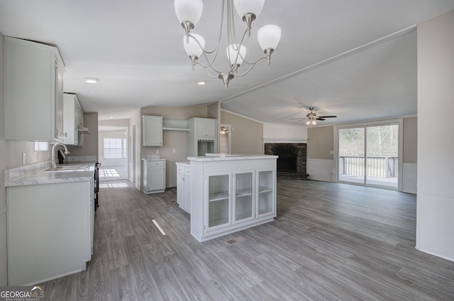 kitchen featuring light wood-type flooring, a fireplace, white cabinets, ceiling fan with notable chandelier, and open floor plan