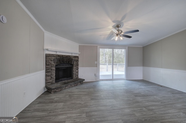 unfurnished living room with a stone fireplace, wood finished floors, a wainscoted wall, and a ceiling fan