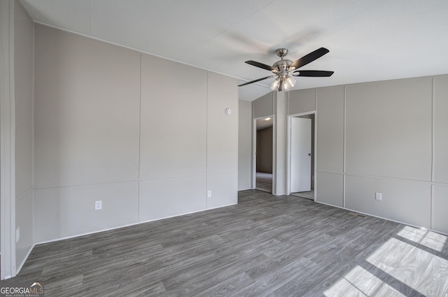 empty room featuring lofted ceiling, wood finished floors, a ceiling fan, and a decorative wall