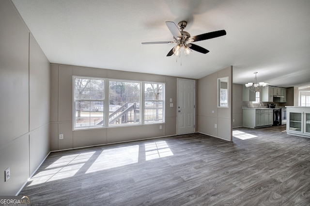 unfurnished living room featuring dark wood finished floors, ceiling fan with notable chandelier, and a sink