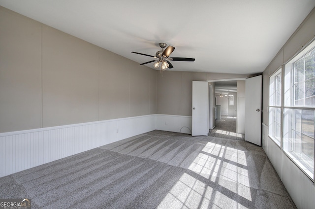 empty room featuring a decorative wall, a ceiling fan, and carpet floors