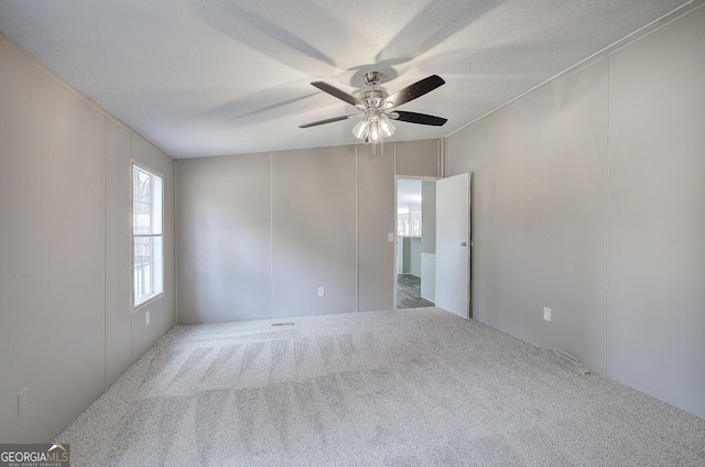 spare room featuring ceiling fan, a decorative wall, carpet, and a textured ceiling