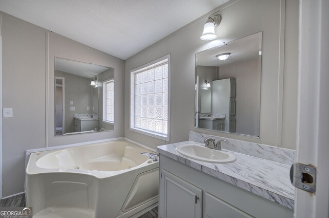 bathroom with a tub with jets, vanity, and vaulted ceiling