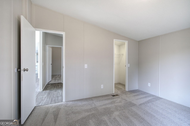 unfurnished bedroom with visible vents, lofted ceiling, a spacious closet, and carpet flooring