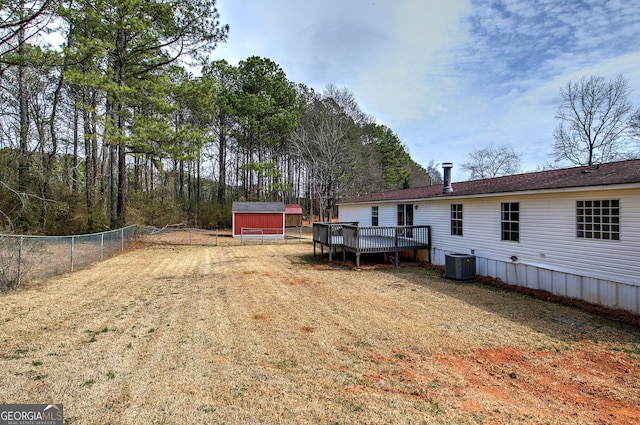 view of yard with fence, a shed, cooling unit, a deck, and an outbuilding