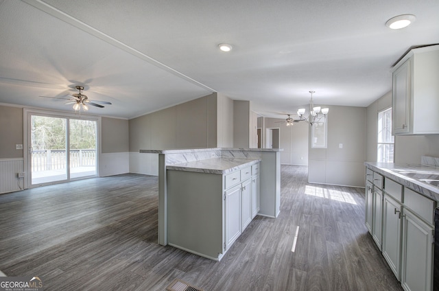 kitchen with a wainscoted wall, ceiling fan with notable chandelier, wood finished floors, open floor plan, and a center island