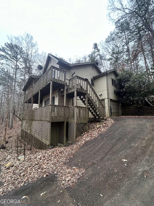 view of front of house featuring stairs, aphalt driveway, an attached garage, and a deck