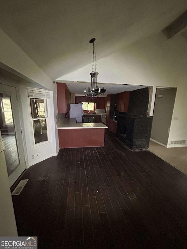 kitchen featuring dark wood-style flooring, light countertops, freestanding refrigerator, vaulted ceiling, and a peninsula