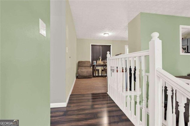 hallway featuring a textured ceiling, wood finished floors, an upstairs landing, and baseboards