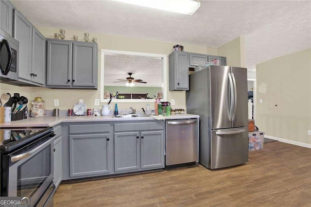 kitchen featuring stainless steel appliances, gray cabinets, a sink, and wood finished floors