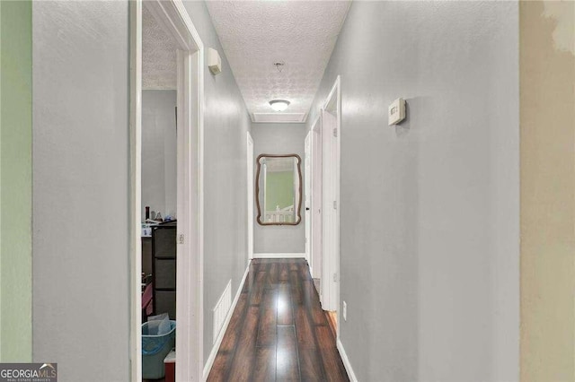 hallway featuring dark wood-style floors, a textured ceiling, visible vents, and baseboards