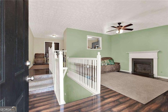 interior space with a textured ceiling, ceiling fan, a fireplace with flush hearth, wood finished floors, and baseboards