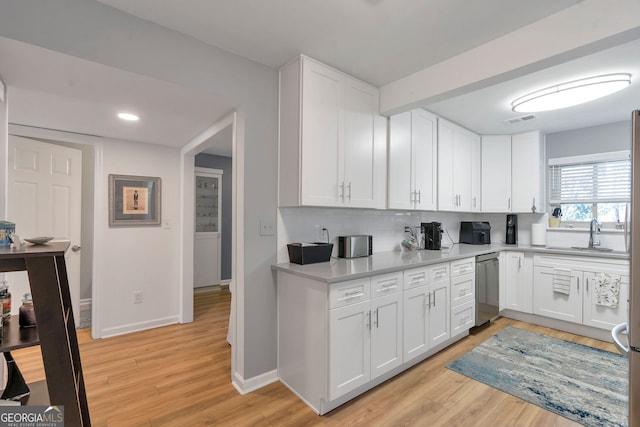 kitchen featuring light countertops, white cabinets, a sink, light wood-type flooring, and dishwasher