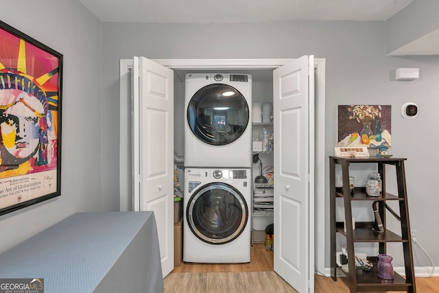 laundry room with laundry area, stacked washer / drying machine, and wood finished floors